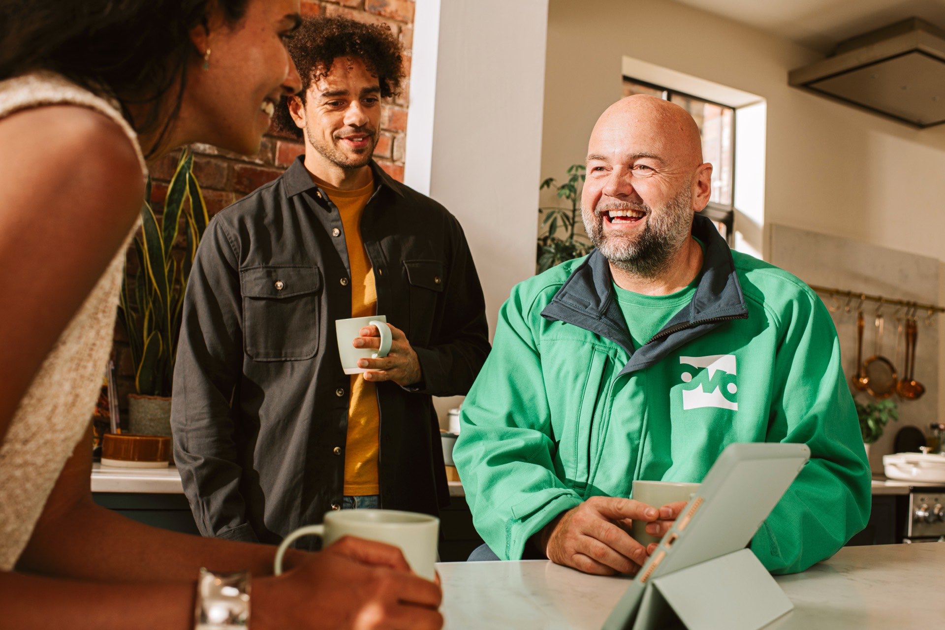 An OVO engineer talking two homeowners through a system on a tablet at a kitchen worktop