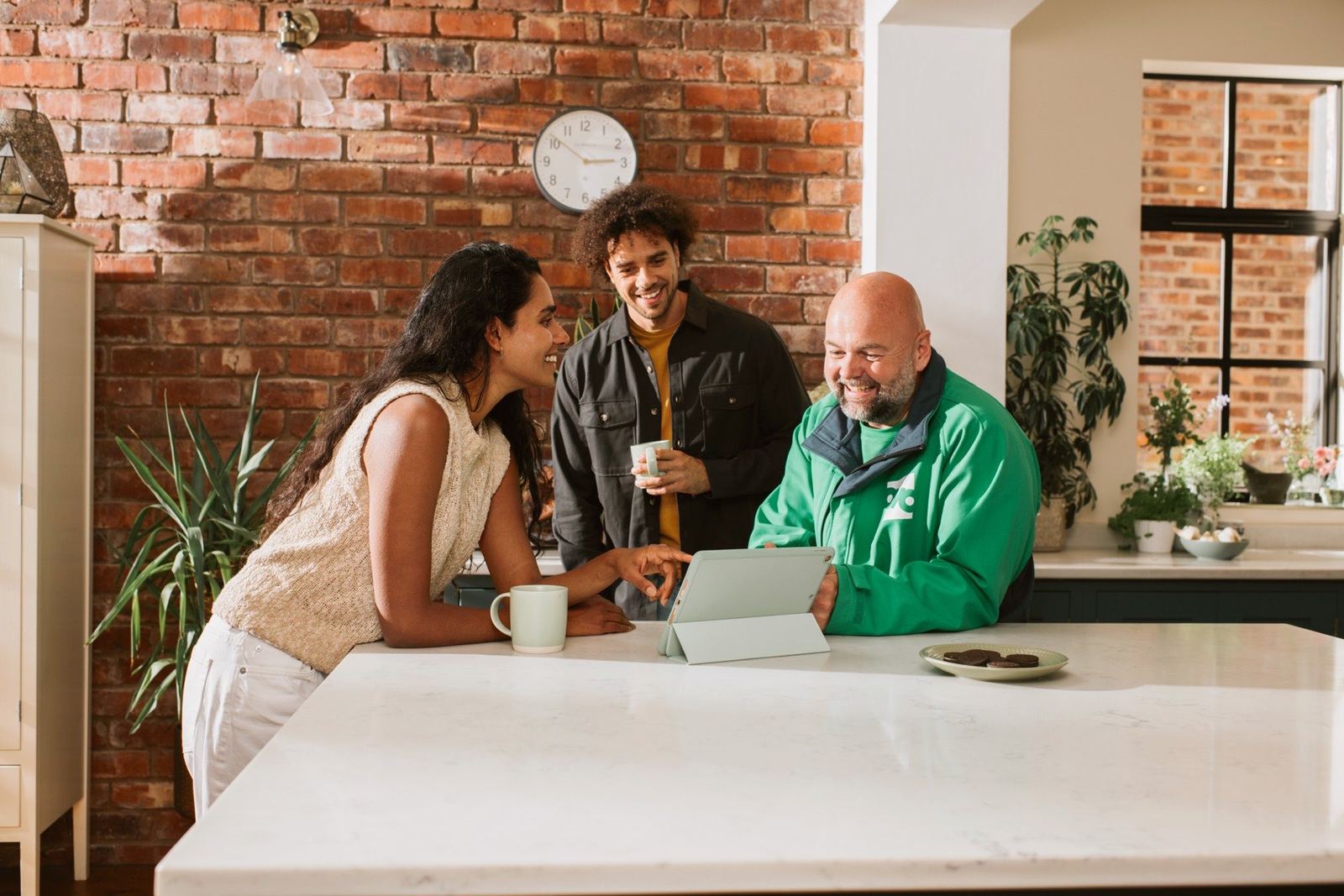 An OVO engineer and two homeowners reading a tablet screen together across a kitchen island